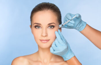 A person receiving a facial injection from a gloved hand against a blue background.