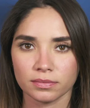 Portrait of a person with long dark hair, brown eyes, and neutral expression, against a blue background.