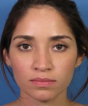 A woman with long dark hair is looking directly at the camera against a plain blue background.