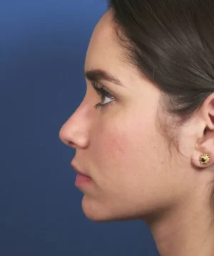 Profile view of a woman against a blue background, showing her face in close-up with dark hair pulled back and wearing sunflower-shaped earrings.