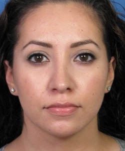 A woman with long dark hair is looking directly at the camera. She has earrings and a neutral expression.