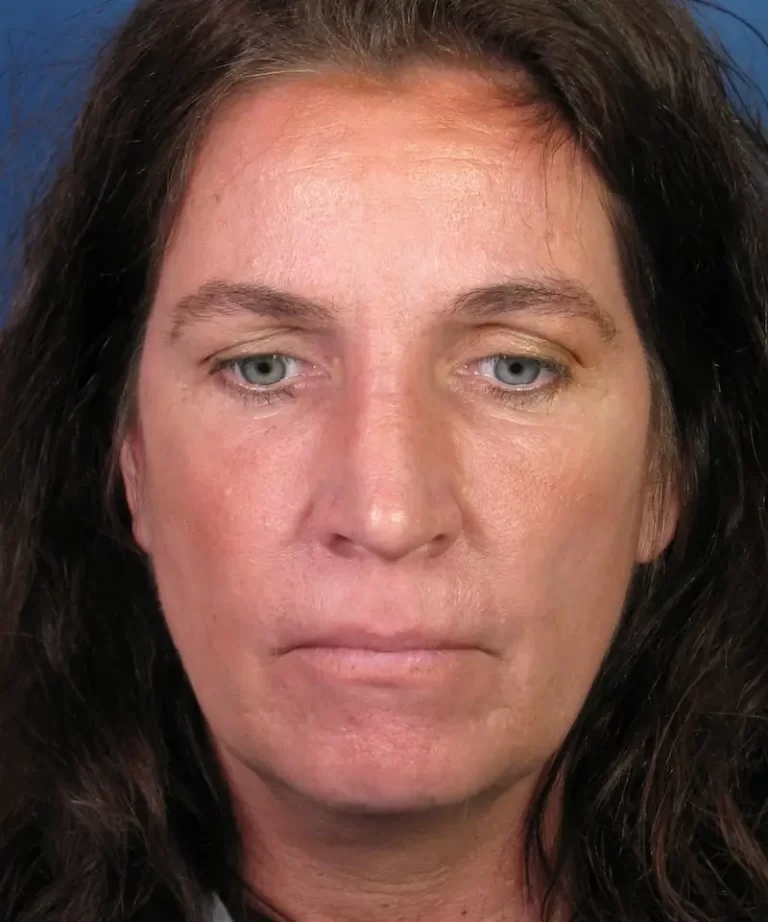 A person with long brown hair and a neutral expression, looking directly at the camera against a blue background.