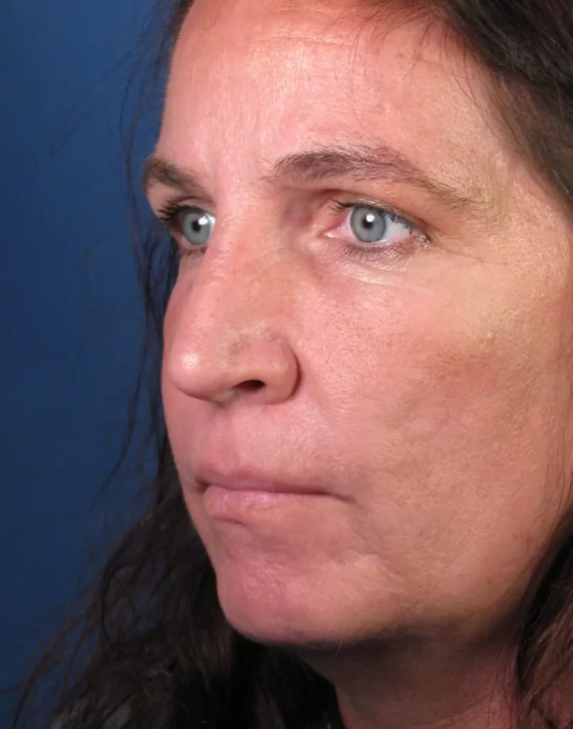 A close-up of a person with long hair and blue eyes, looking to the side. The background is a solid blue color.