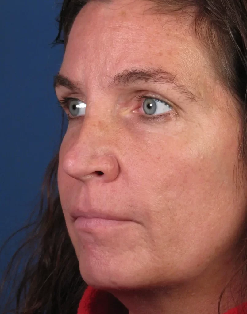 A woman with long brown hair and blue eyes looks to the side against a blue background.