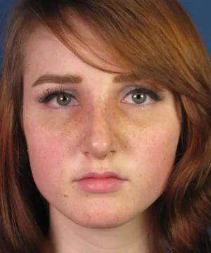 Close-up of a person with auburn hair, green eyes, and freckles, looking directly at the camera.