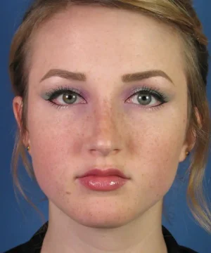 A person with green eyes and light makeup looks directly at the camera against a blue background.