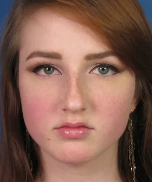 Young woman with red hair and freckles looking directly at the camera. She is wearing makeup and long earrings.