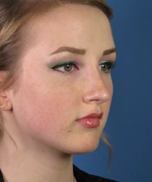 A person with light skin and light-colored eyes gazes to the side. They have makeup on, including eye shadow, eyeliner, and lipstick. The background is blue.