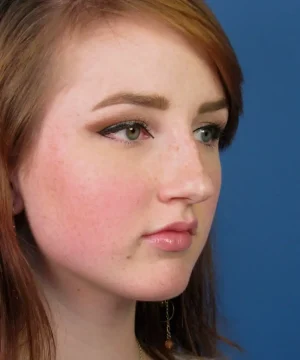 A person with long brown hair and subtle makeup looks away from the camera against a blue background.