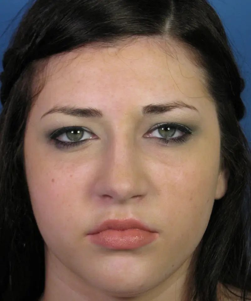A woman with long dark hair and green eyes is looking directly at the camera against a blue background.