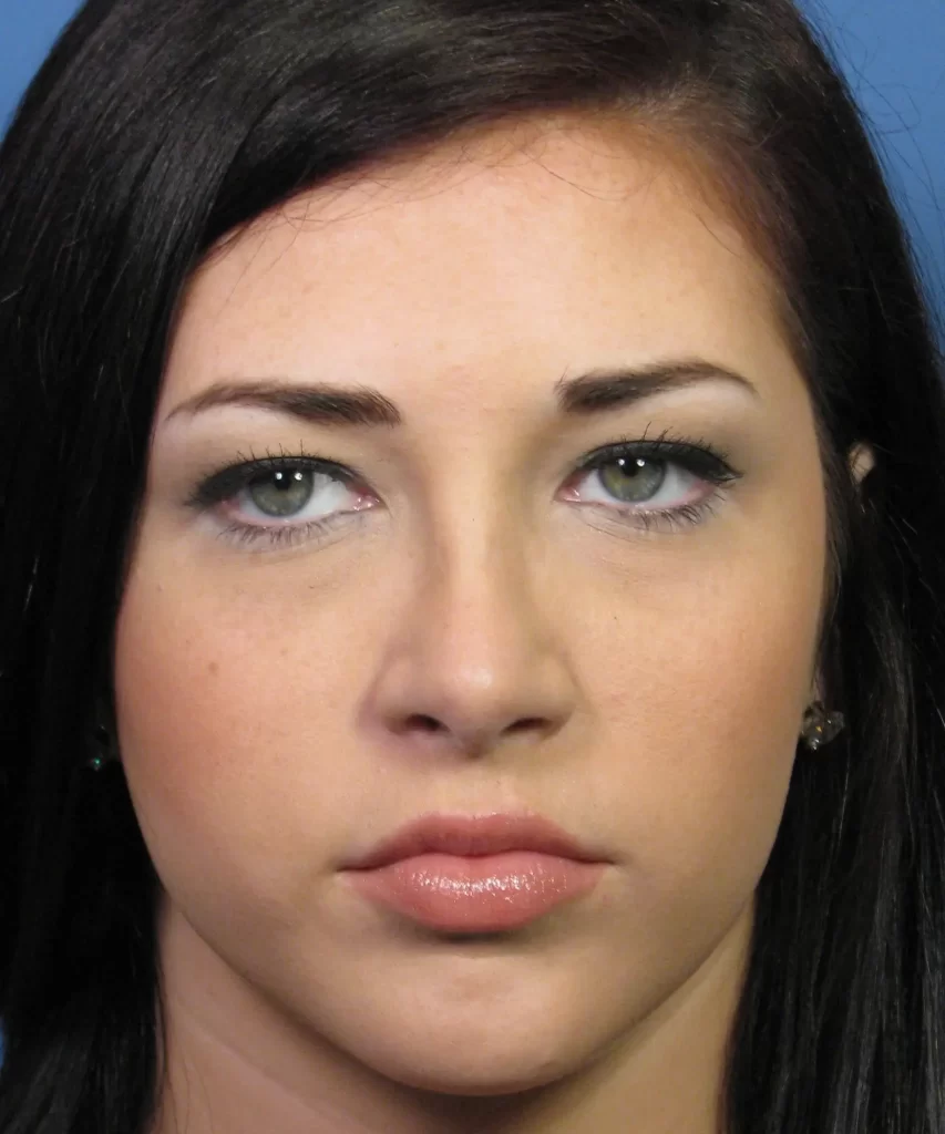 A woman with long dark hair and neutral expression is looking directly ahead against a plain blue background.