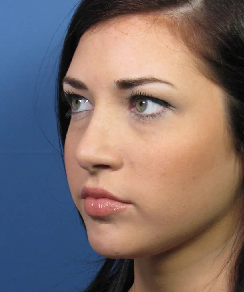 Close-up of a person with long dark hair and green eyes gazing forward. Blue background.