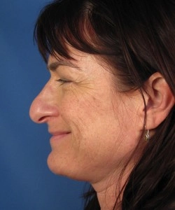 Side profile of a woman with brown hair, smiling, against a blue background.