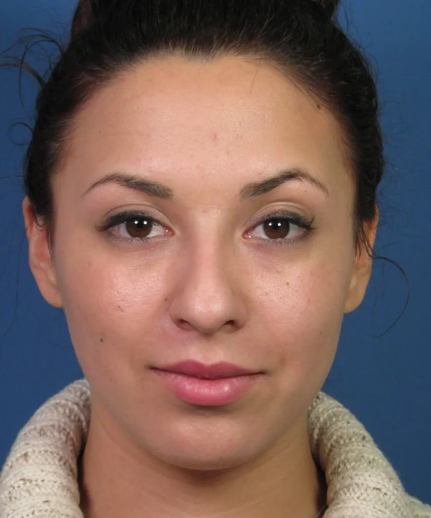A woman with a neutral expression facing forward against a blue background, wearing a light-colored turtleneck sweater.
