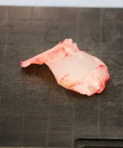 A raw piece of fish on a dark, grid-patterned surface.