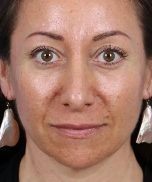 A woman with long earrings, natural makeup, and a neutral expression looks directly at the camera.