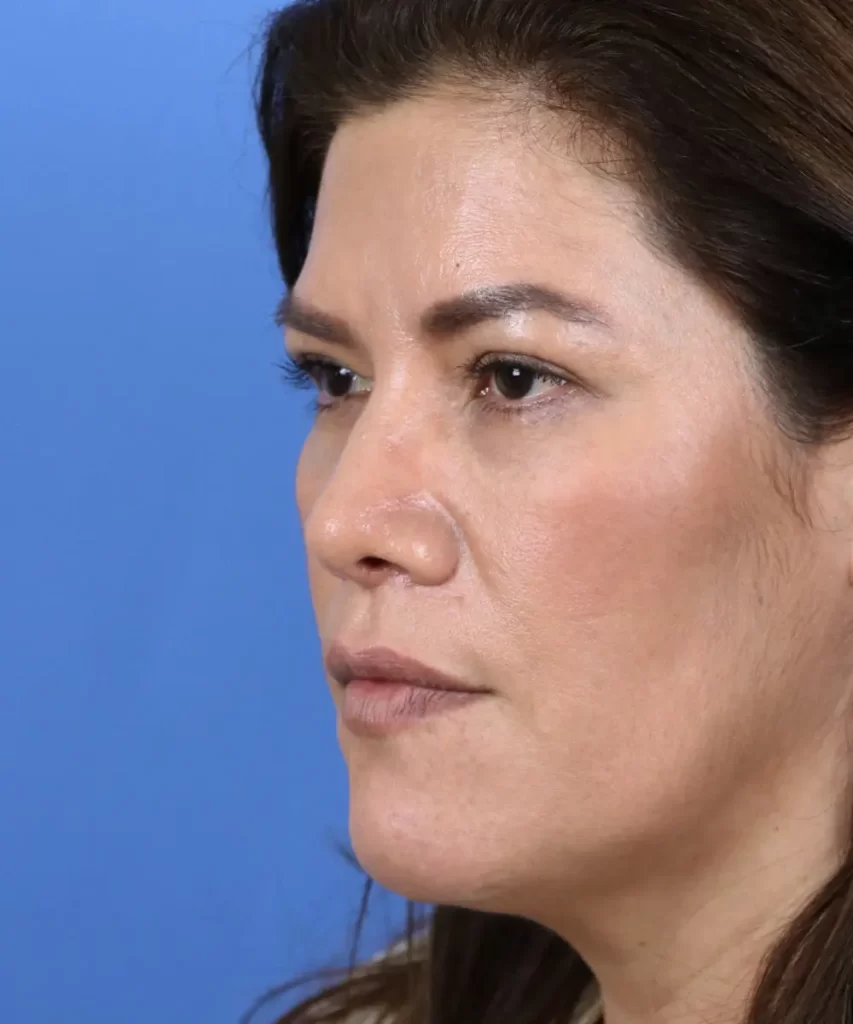 A woman with long dark hair is staring to the right against a blue background.
