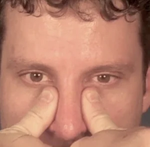 Person applying pressure on the sides of their nose with their thumbs.