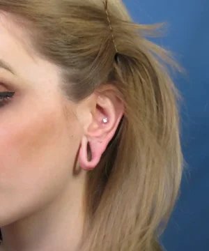 Person with blonde hair showing a stretched earlobe and two piercings on the ear.
