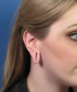 A woman with long hair has stretched earlobes and is facing sideways against a blue background.