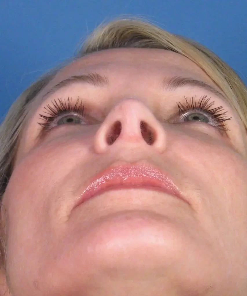 Close-up of a person's face looking up against a blue background, highlighting their eyelashes and nostrils.