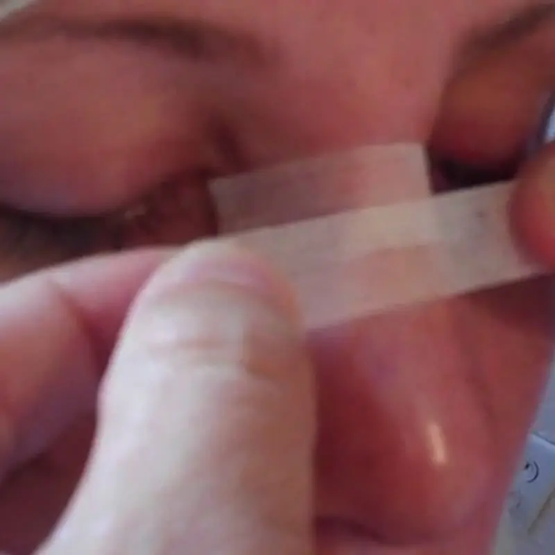 A person applying medical tape over their closed eyelid.