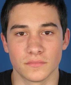 A young person with short dark hair and a neutral expression is shown against a solid blue background.