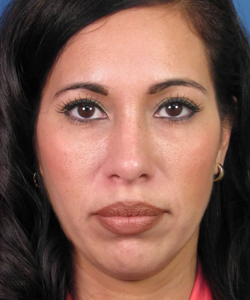 Woman with long dark hair, earrings, and a pink top, looking directly at the camera against a blue background.